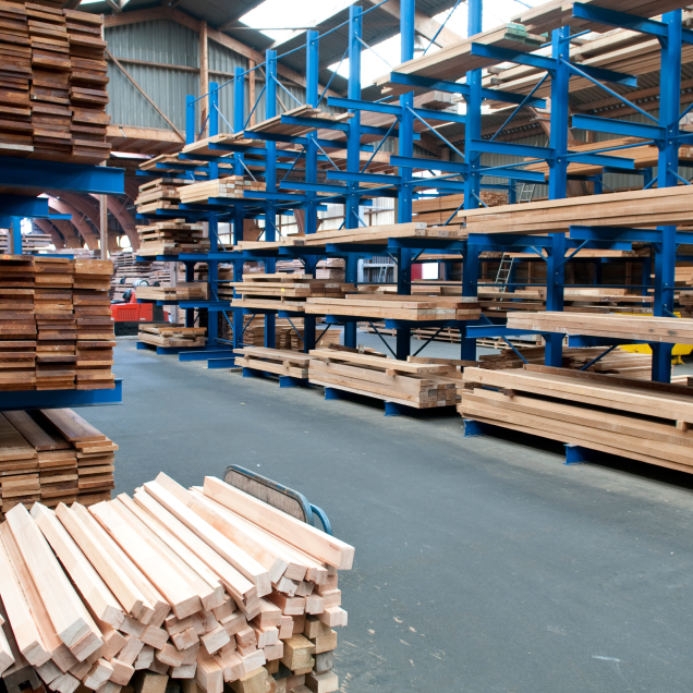 The inside of a lumber room, with blue shelving holding stacks of different wood.